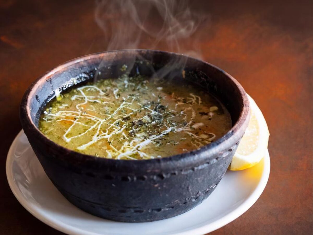 A steaming dark clay bowl of golden begova čorba with a slice of lemon, at Aljina kafana in Tuzla
