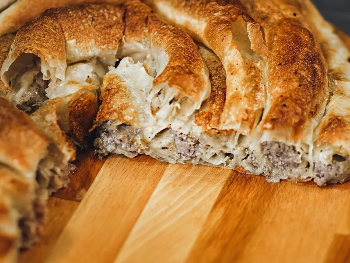 A coil of burek cut open on a wooden board, the minced meat filling showing