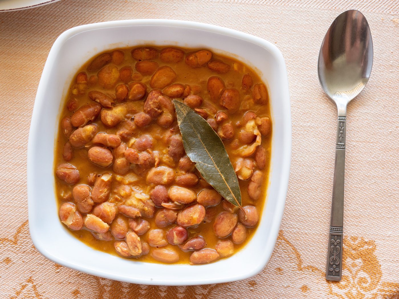 A bowl of pinto bean stew with a bay leaf and a spoon