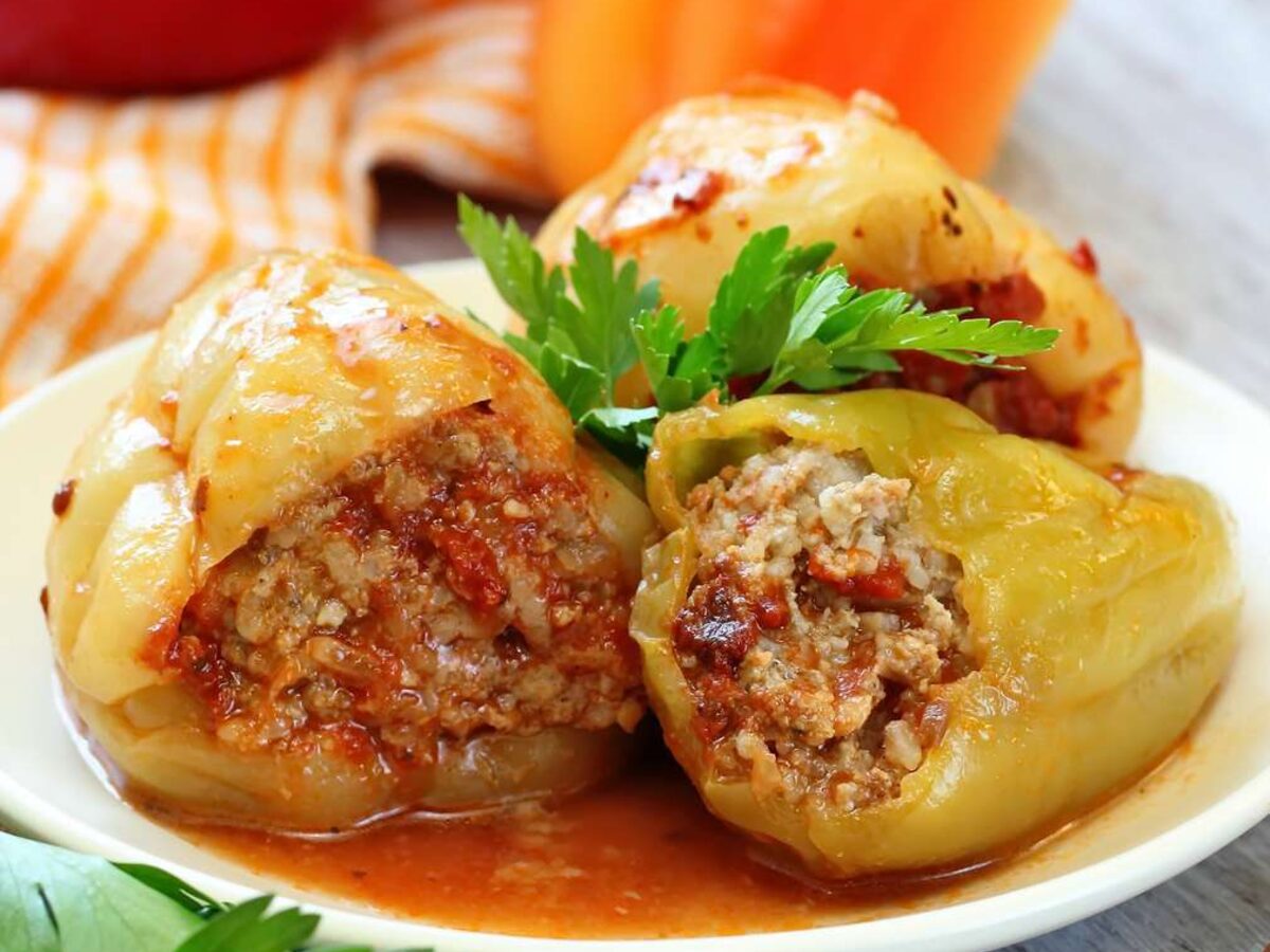 Two pale green peppers cut open to show a meat and rice filling, in tomato sauce with parsley
