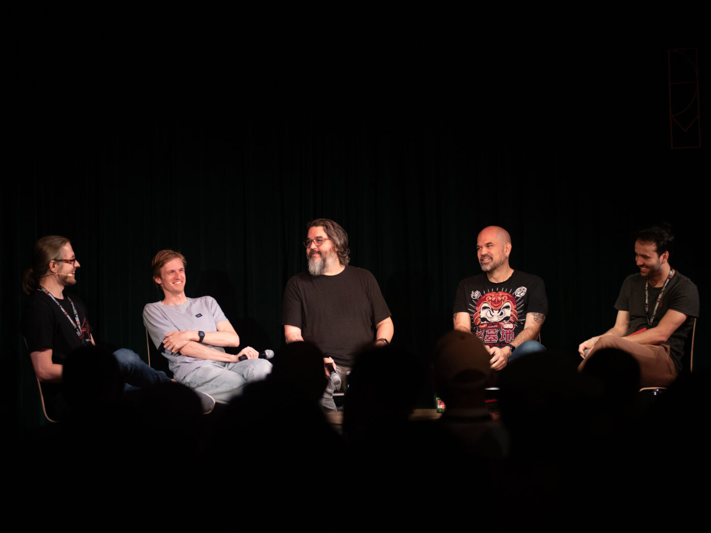 Five people seated in a row on a dark stage, laughing, for the evening panel