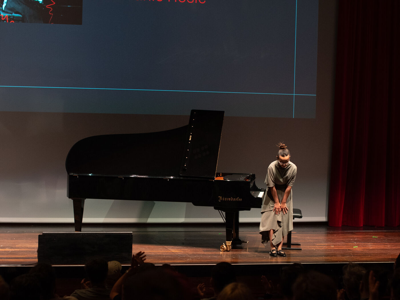 A musician bowing beside a grand piano on the stage