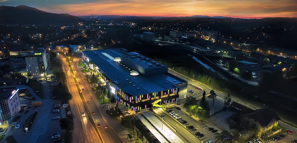 An aerial evening view of the Bingo City Center building beside the main road, with the city lights behind