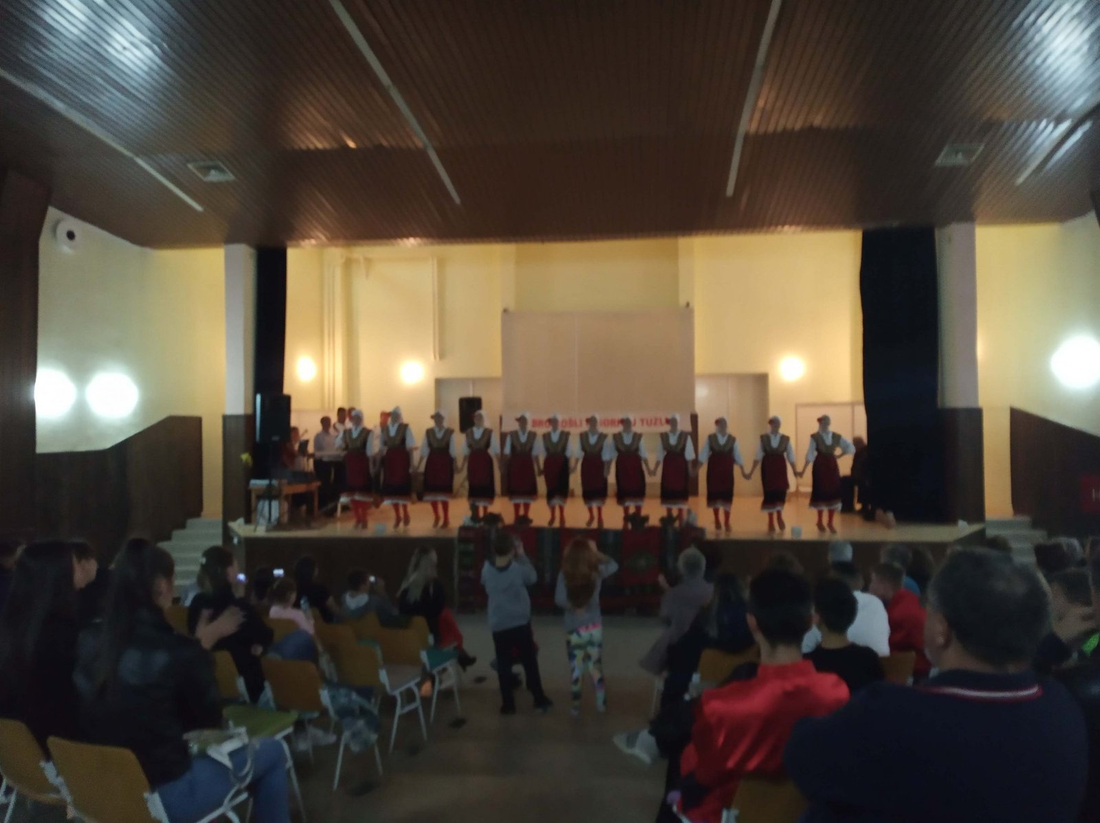A folk dance group in costume on the stage of the house's big hall during a concert in October 2019, with the audience seated in front