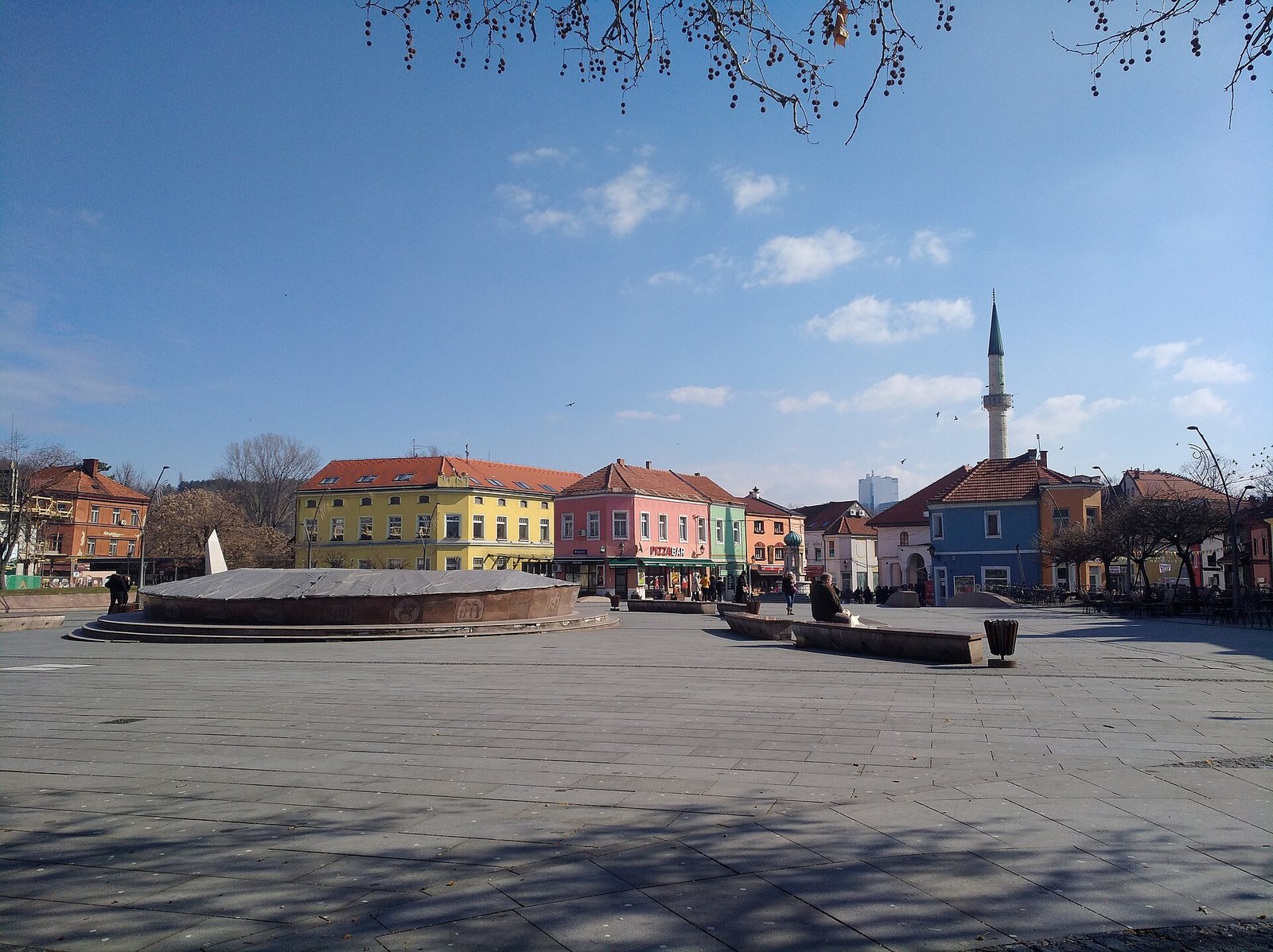Freedom Square on a sunny day: wide paving, the round fountain and the mosque minaret behind the houses