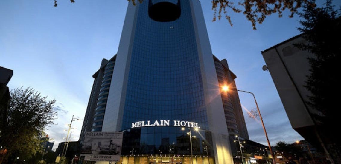 The tall glass front of Hotel Mellain lit up at dusk
