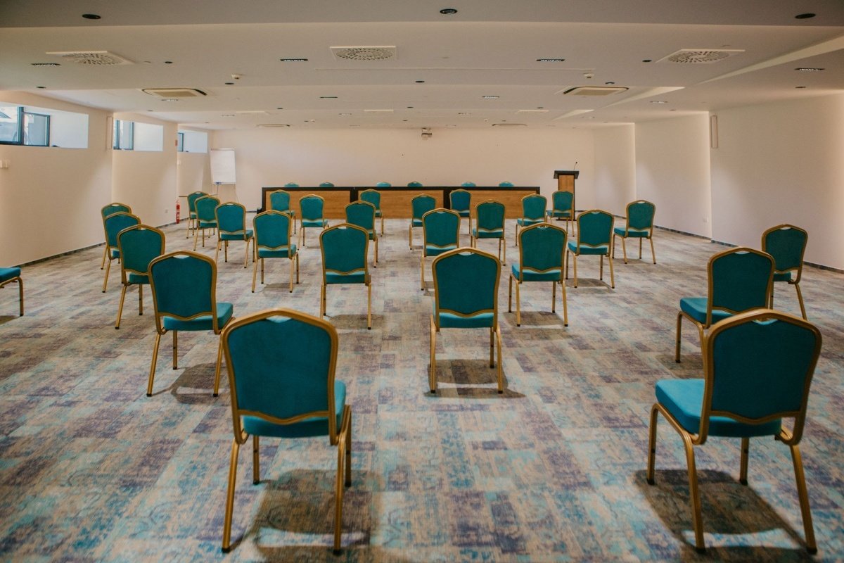 The conference hall of Hotel Salis, set with spaced-out green chairs and a head table