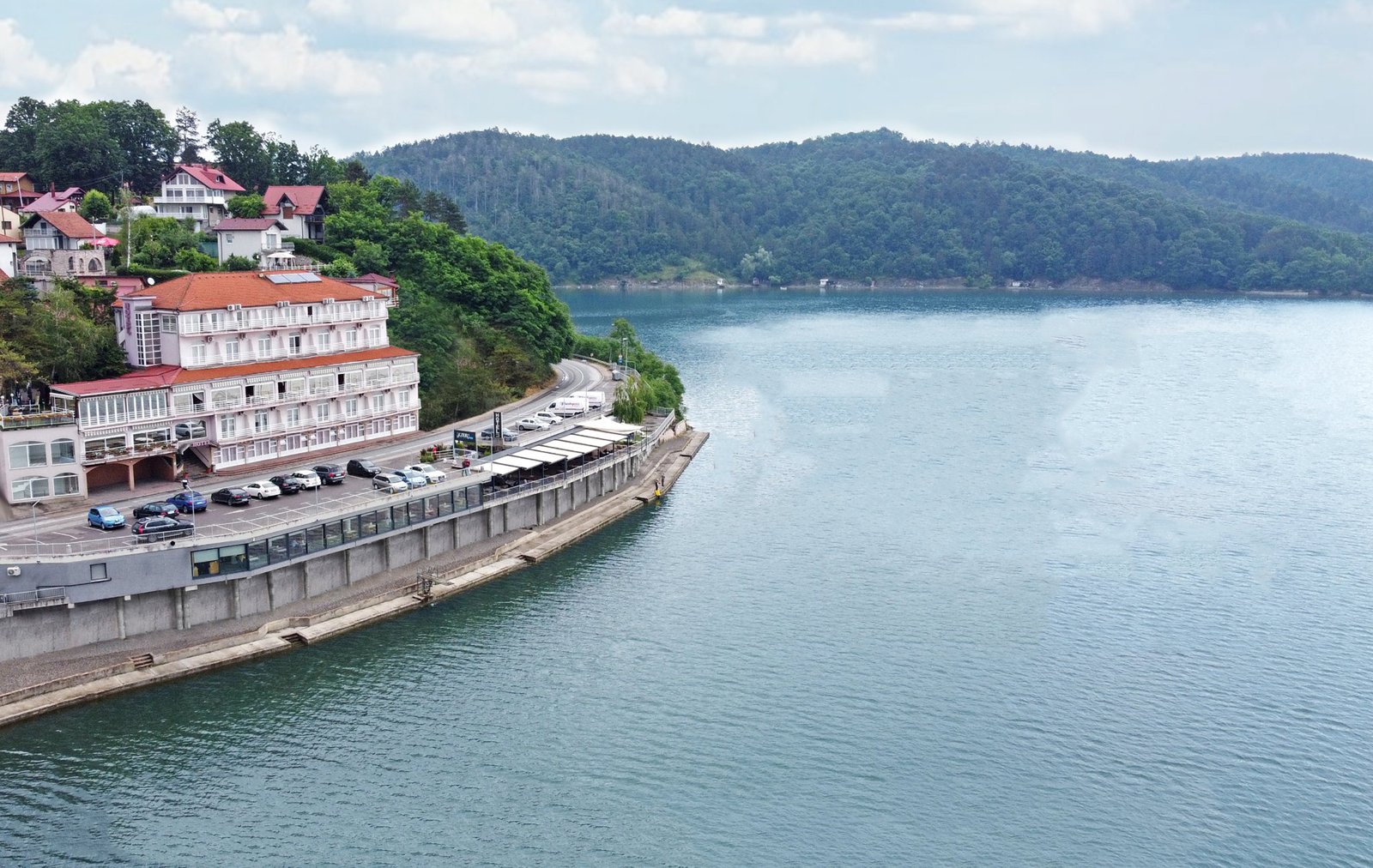 An aerial view of the hotel building on the shore of Lake Modrac, with wooded hills behind