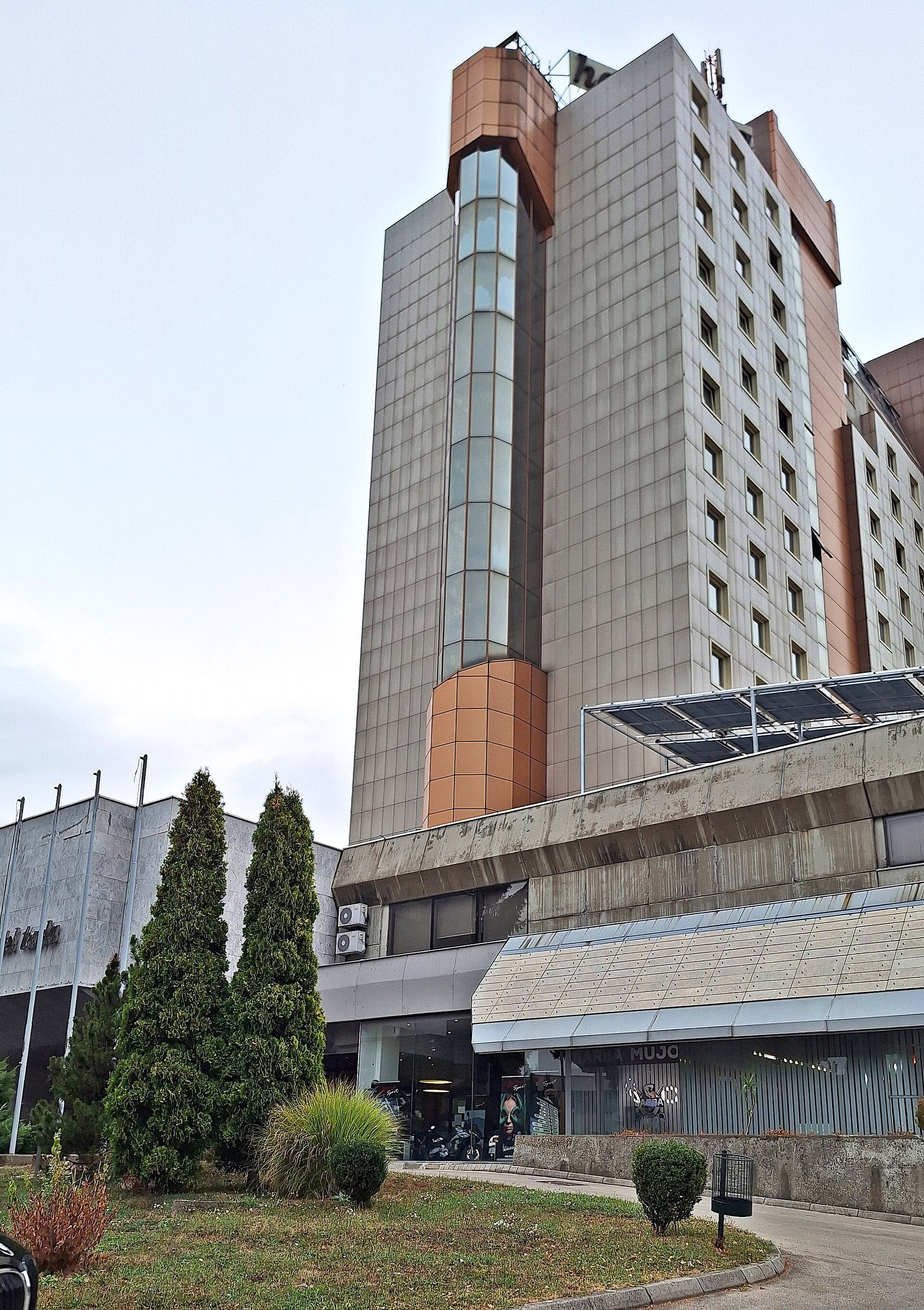 Hotel Tuzla, a tall 1980s tower with a glass stair column, above a low entrance wing