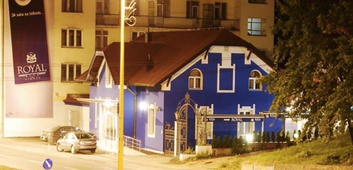 Motel Royal, a blue house with a lit garden, at night