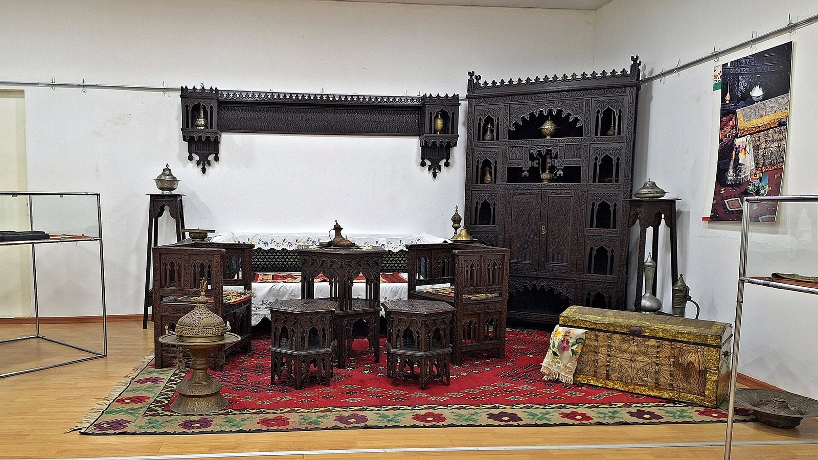 The ethnographic corner of the museum's exhibition, with a carved wooden cabinet, low wooden tables and stools, copper vessels and a red carpet