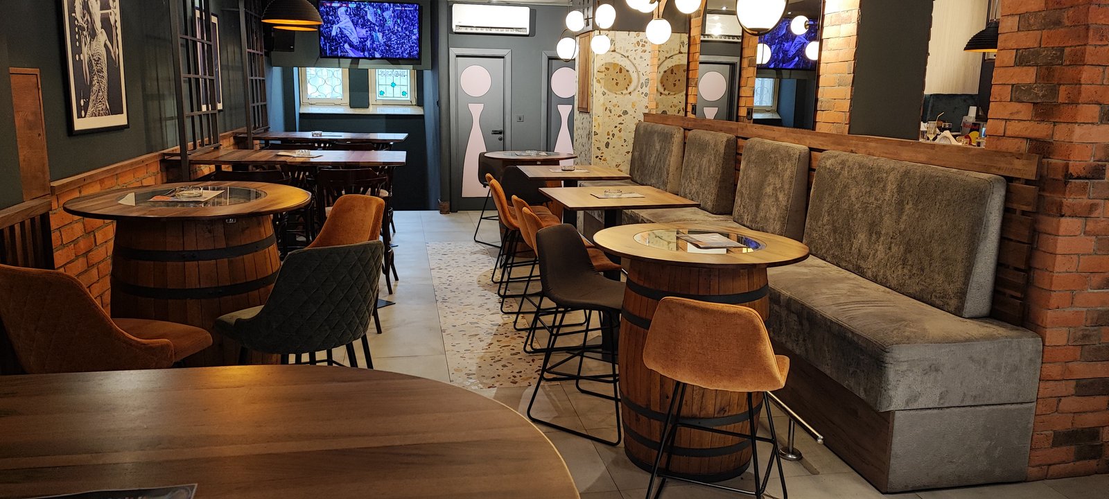 The empty interior of Nardi Pub with barrel tables, high stools, a long grey bench, brick pillars and wall screens