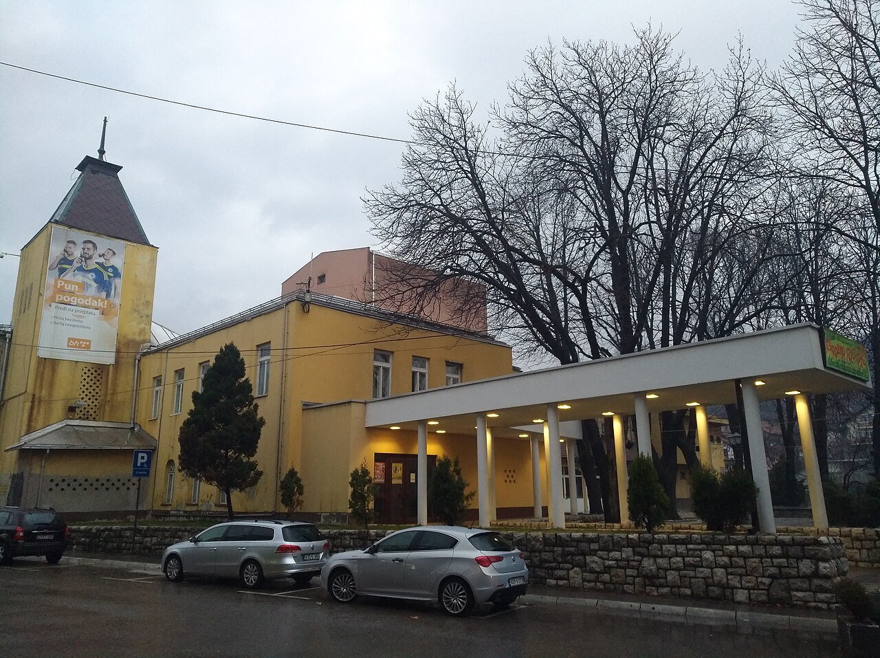 The yellow National Theatre building with its tower and a covered entrance, cars parked in front