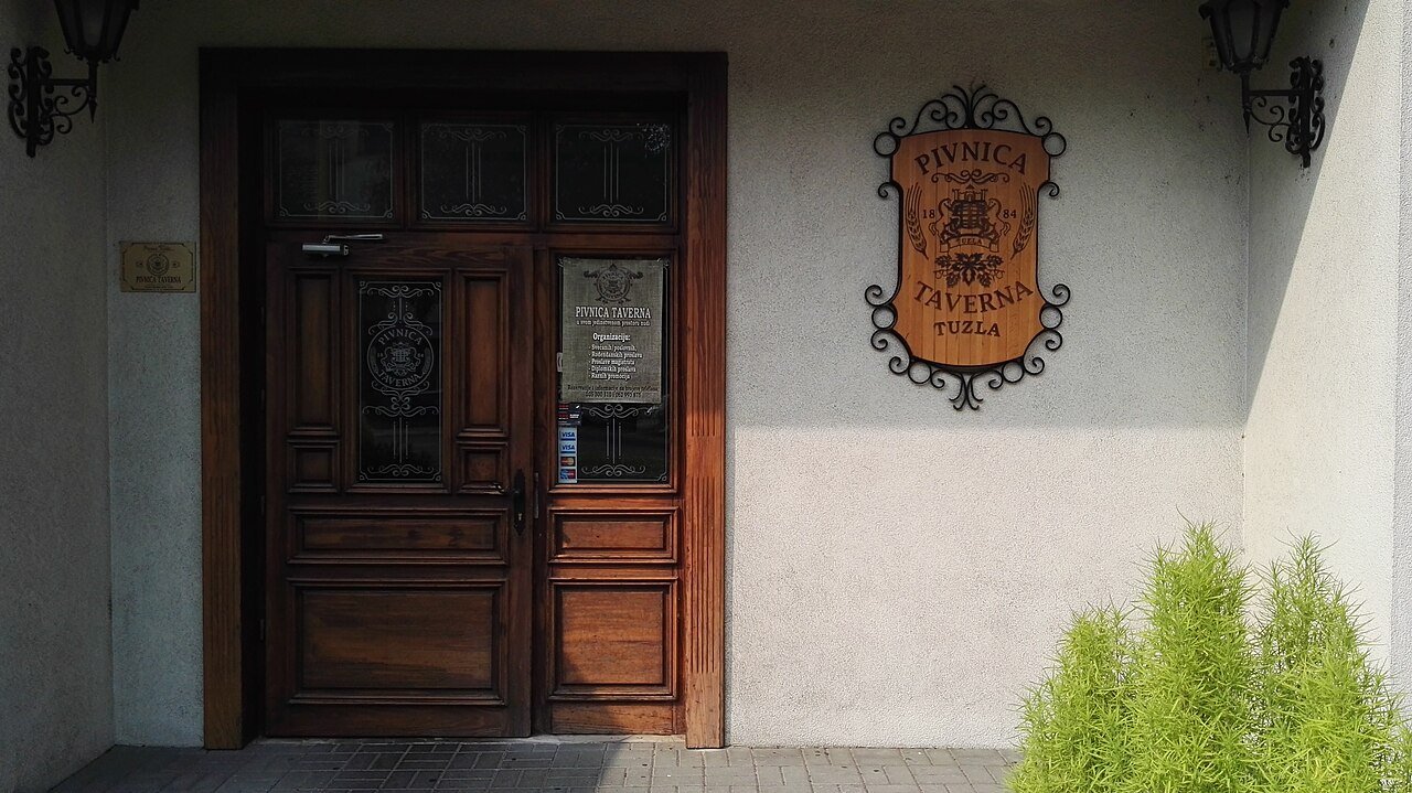 The wooden double door of Pivnica Taverna with the brewery crest on the wall beside it