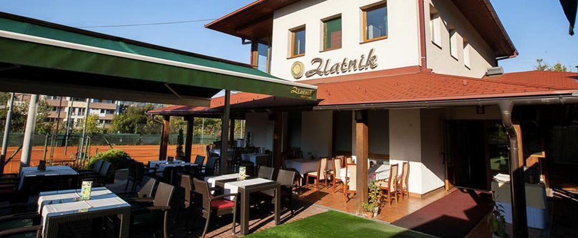 Restoran Zlatnik: a white house with a red roof and a garden of tables under green awnings