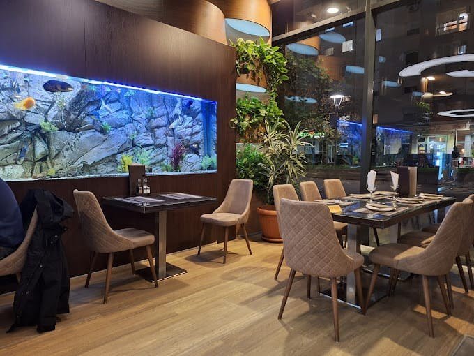 The restaurant's dining area with a long built-in aquarium on the wall, upholstered chairs and laid tables, with no people