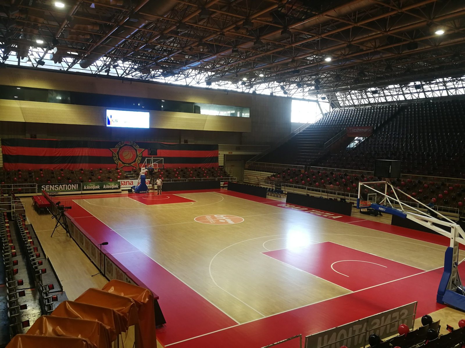 The empty big hall with its red and wooden basketball court, steep stands and roof trusses