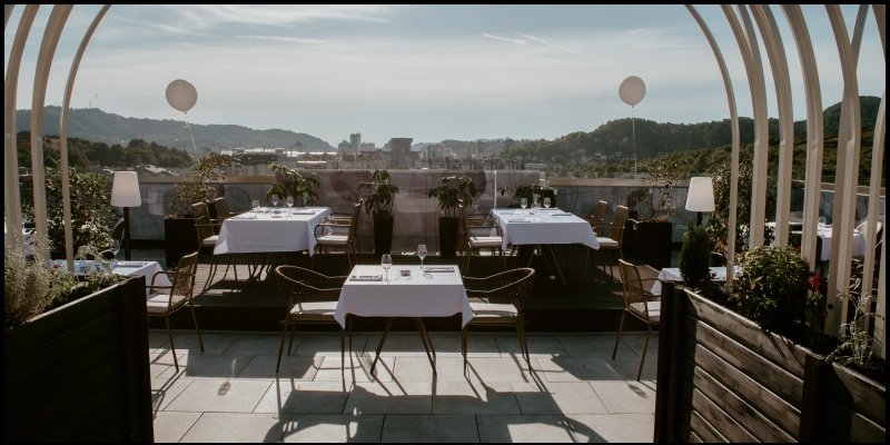The roof terrace of The Loft, with set tables, arches and the hills of Tuzla behind